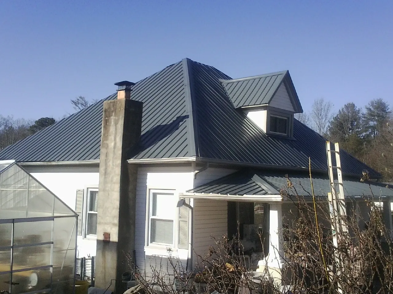 Dark blue standing seam metal roof on a white farmhouse with dormer — Slate & Tile Roof Repair by Roofing Brothers in Sherman