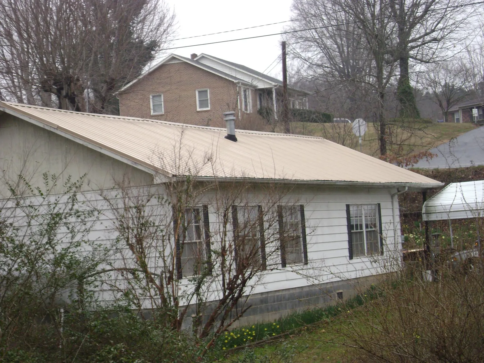 Tan metal roof on a white sided house set into a hillside — Commercial Roofing by Roofing Brothers in Sherman