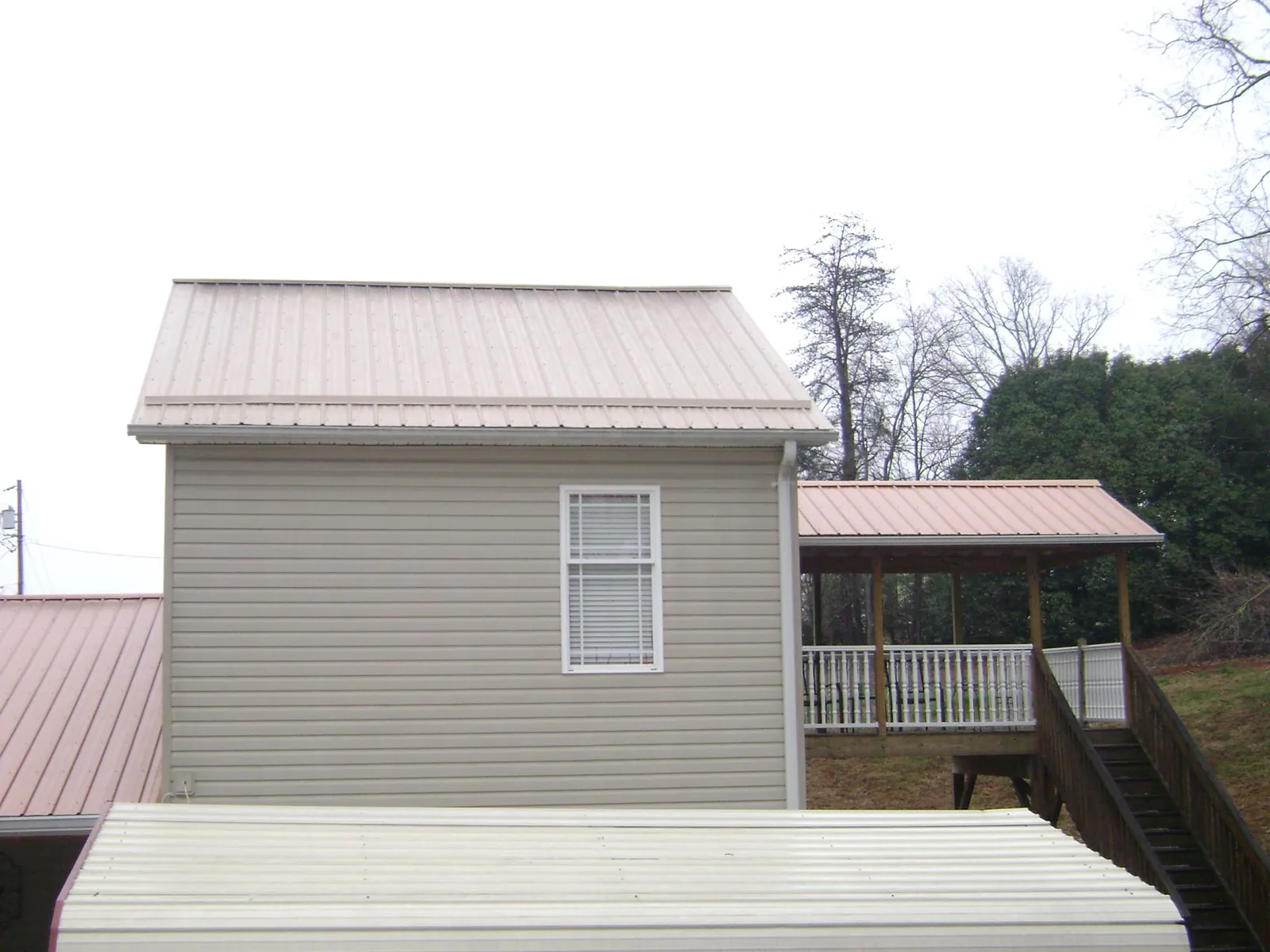 Tan metal roofs on a two story addition and attached porch, from a Roof Replacement job in Sherman